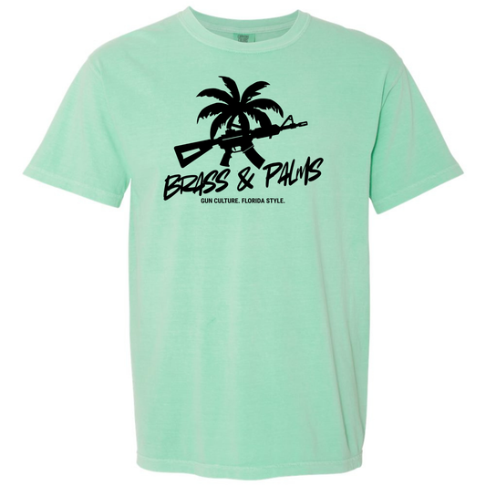 An Island Reef green short-sleeve t-shirt with a black graphic on the chest featuring a palm tree, rifle silhouette, and the text 'BRASS & PALMS' and 'Gun Culture. Florida Style.